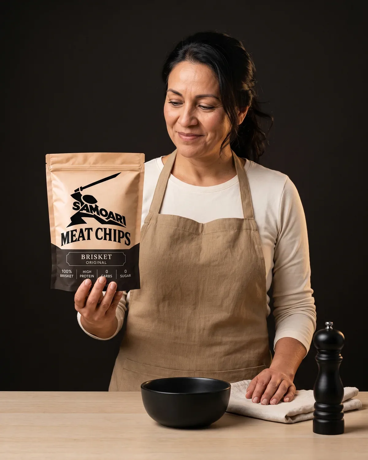 A cook at a kitchen counter holding a bag of Samoari Meat Chips, Brisket Original